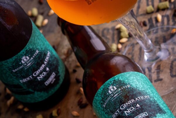 Sfeervolle productfoto van ambachtelijk bier van Bronckhorster Brewing Company met hoppellets en diverse mouten gelegen op een houten bourbon vat