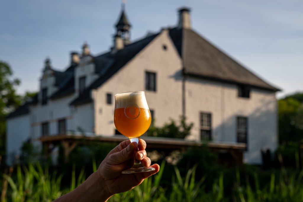 iconisch sfeerbeeld voor Hop in 't Slot bierfestival, proefglas met helder bier met op de achtergrond het kasteel Slot Doddendael